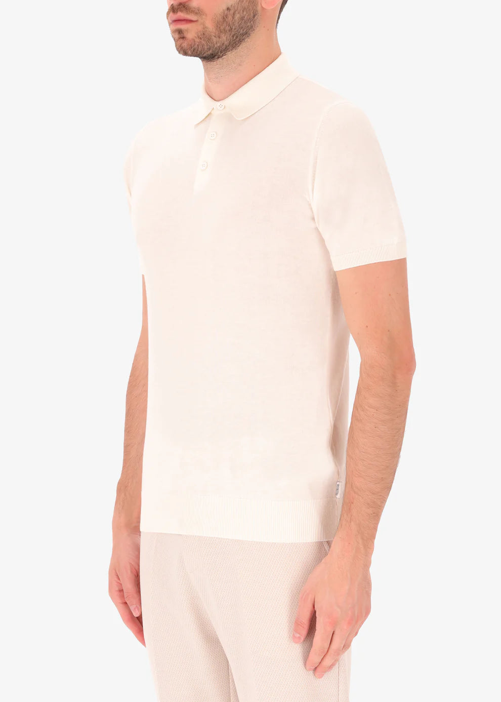 A side facing picture of a model wearing a knitted white polo from Distretto 12.