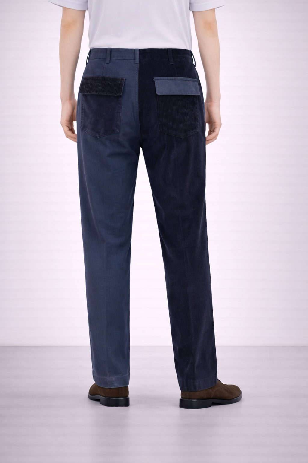 A back angled image of a model wearing Germano 1952 blue trousers with one leg cotton & the other in corduroy.