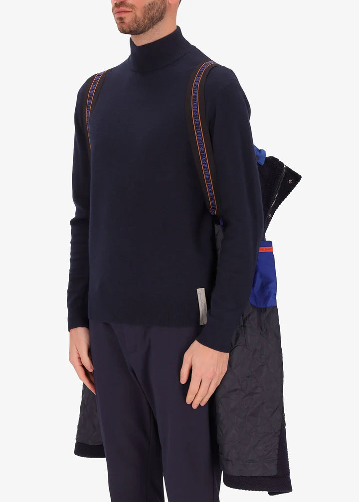 An image of a model wearing a Distretto12 parka in blue with light blue hood by the suspenders.