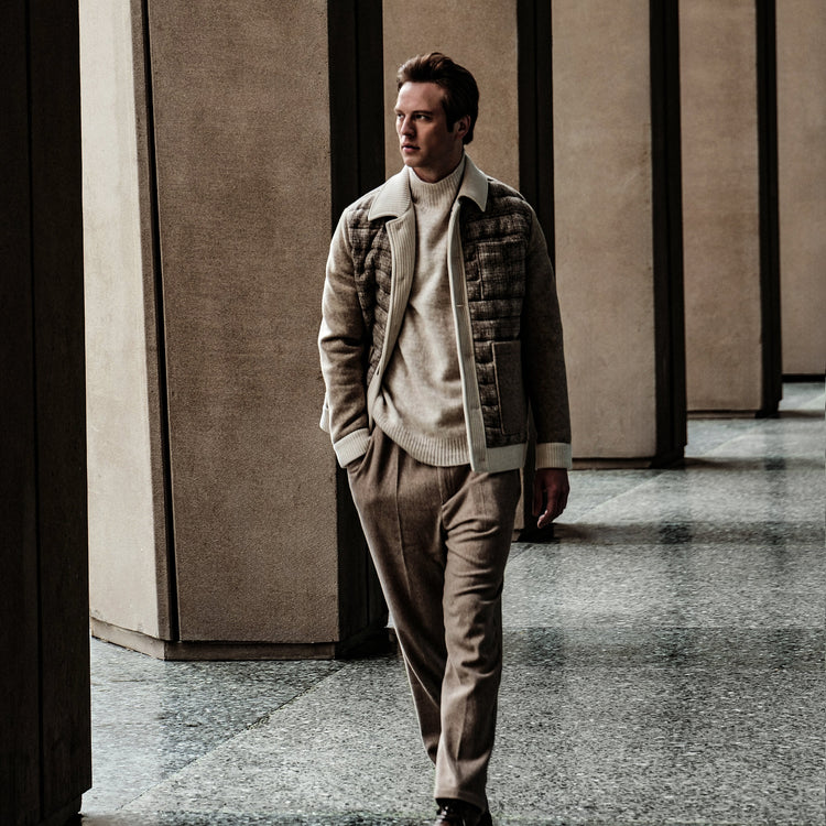 A man walking while wearing corduroy trousers with a tartan coat & cream knitwear