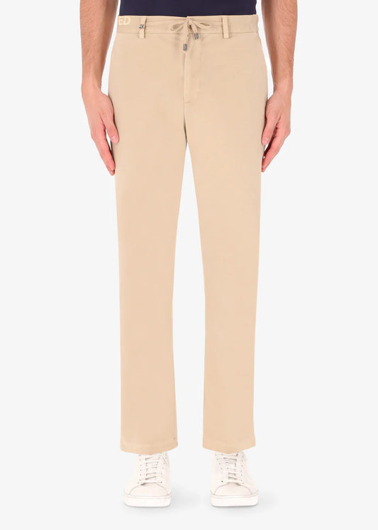An image of a model wearing reshaped chinos in tan from Distretto 12.