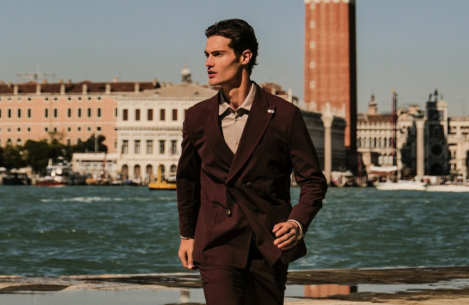 Man wearing a Distretto12 Double breasted suit standing by a waterfront with buildings in the background
