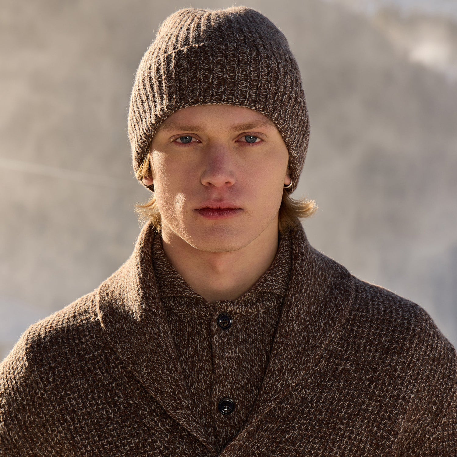 Man wearing a brown knitted hat and knitwear against a blurred natural background
