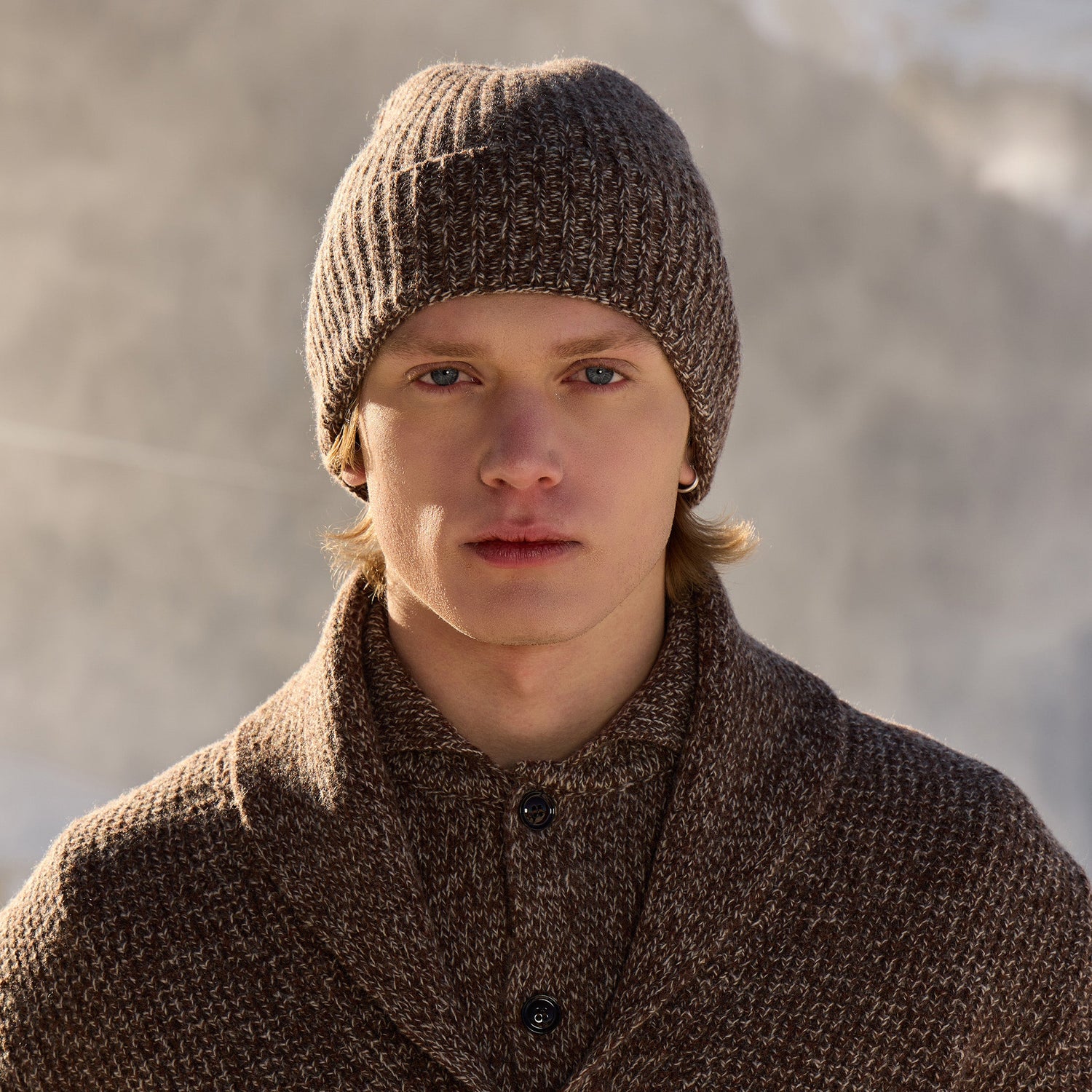 Man wearing a Wool&Co brown knitted hat and Wool&Co cardigan against a blurred natural background