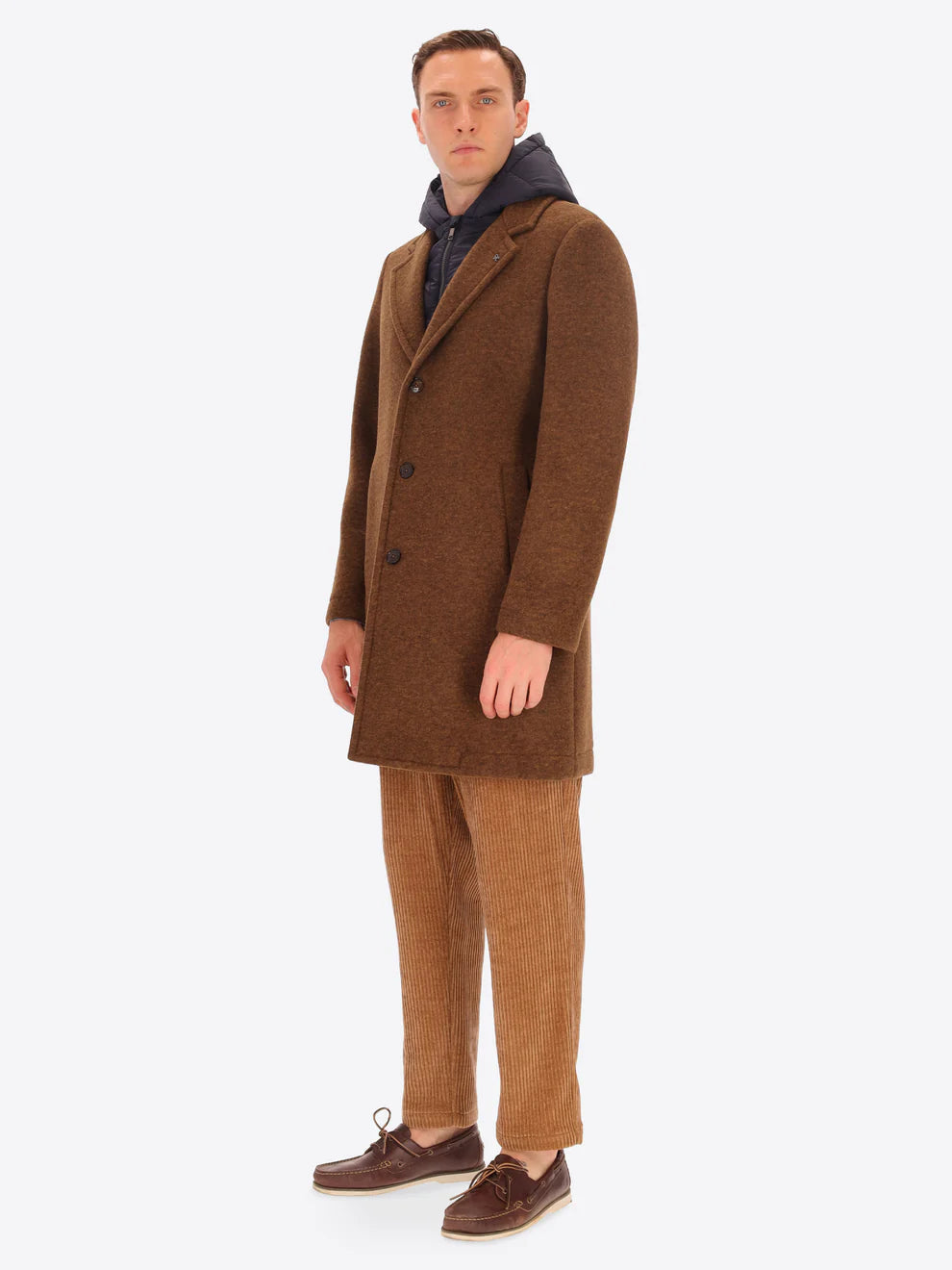 Male model wearing tobacco coloured overcoat by distretto12 with detachable hood with corduroy trousers