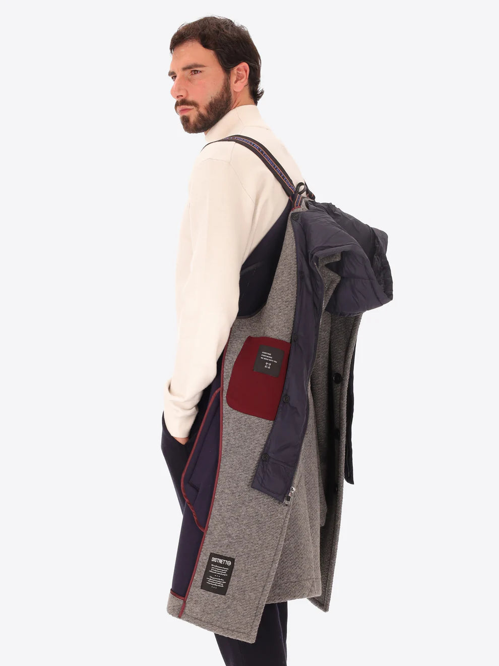 Male model wearing grey overcoat with detachable hood insert by distretto12 with straps hung from shoulder