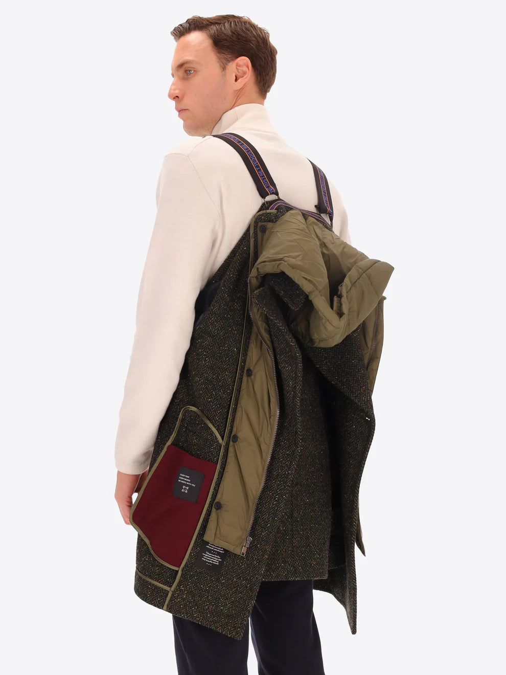 Male model wearing green peacoat with detachable hood insert by distretto12 with micro pattern hung over shoulder with straps