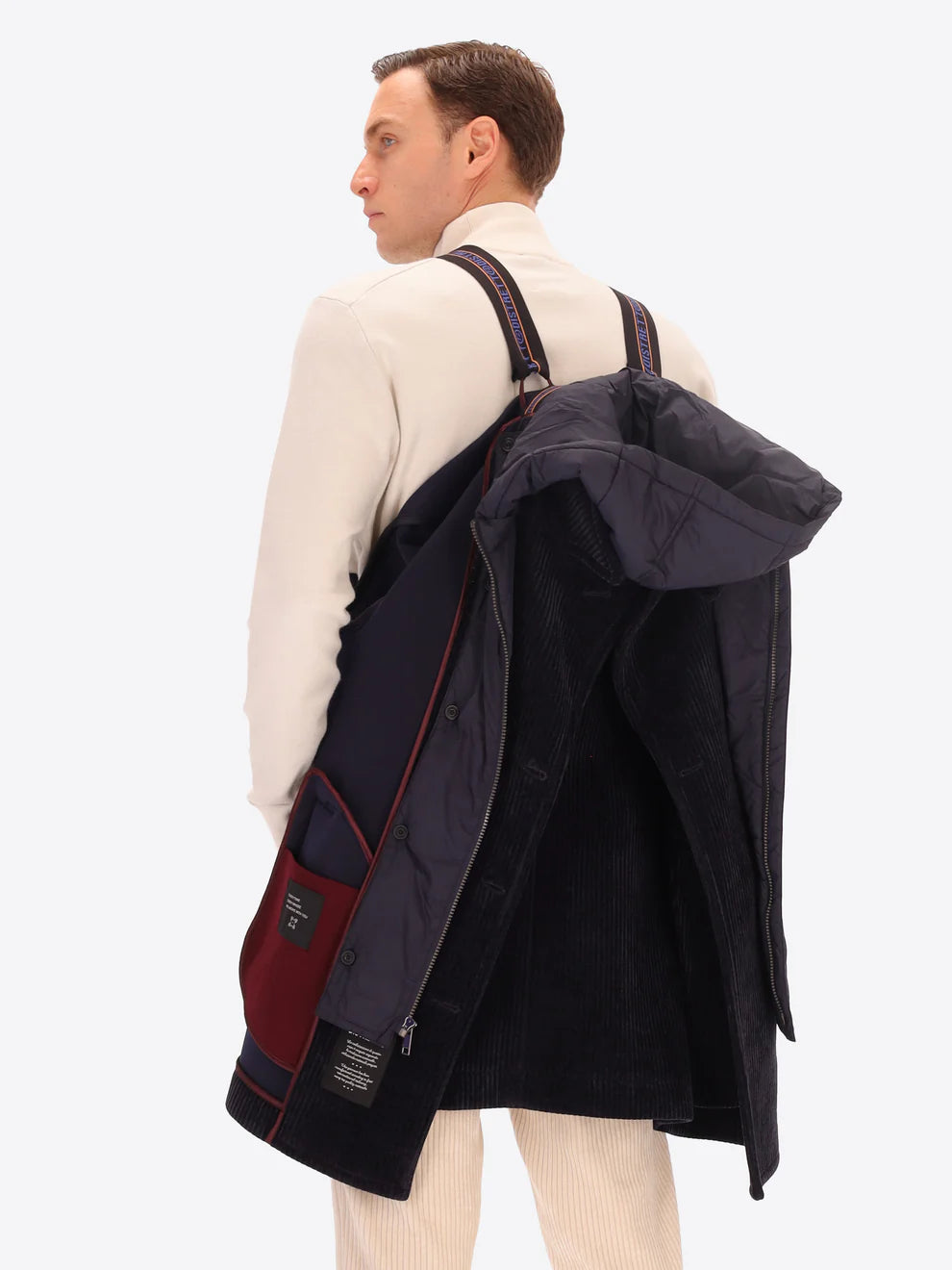 Male model wearing navy corduroy peacoat with detachable hood insert by distretto12 with straps hung over shoulder