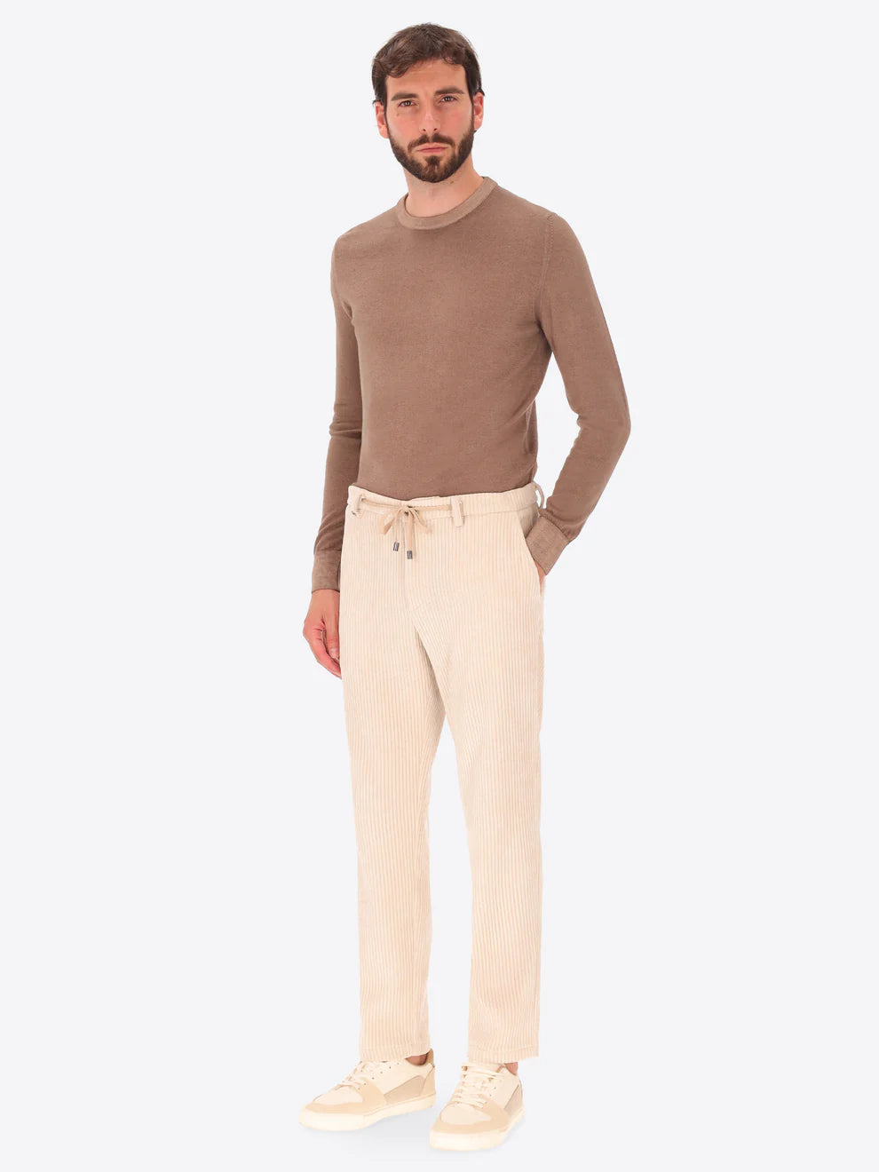 Cream colour corduroy style Distretto12 trousers on a male model paired with brown crewneck knitwear