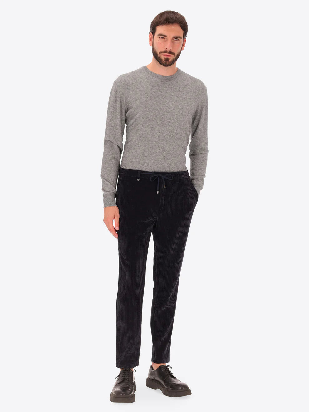Navy corduroy style Distretto12 trousers on a male model paired with grey crewneck knitwear