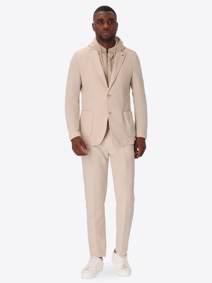 A picture of a model wearing Distretto 12 Jacket Rufino with hood paired with off white trousers and tennis shoes