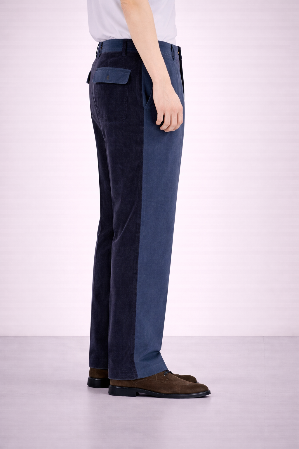 A side on image of a model wearing Germano 1952 blue trousers with one leg cotton & the other in corduroy.